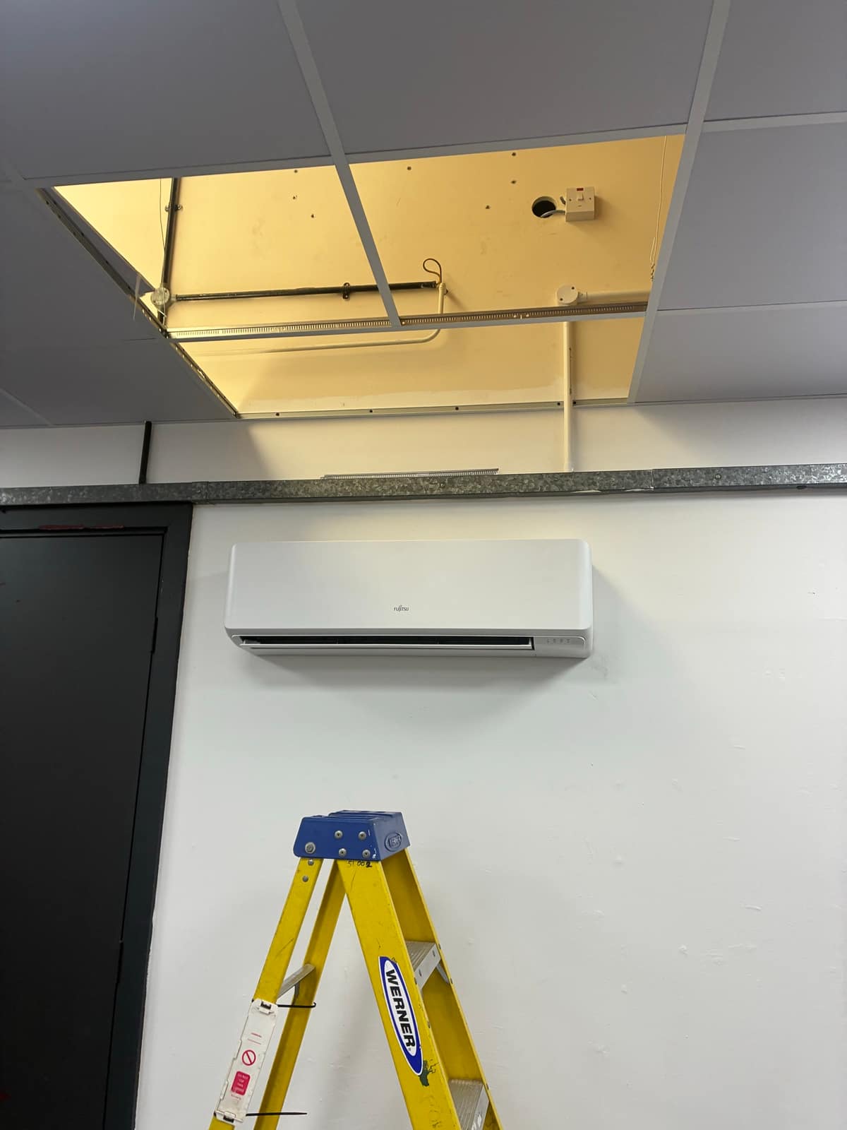 Wall-mounted air conditioning unit with ceiling void open during an F-Gas service