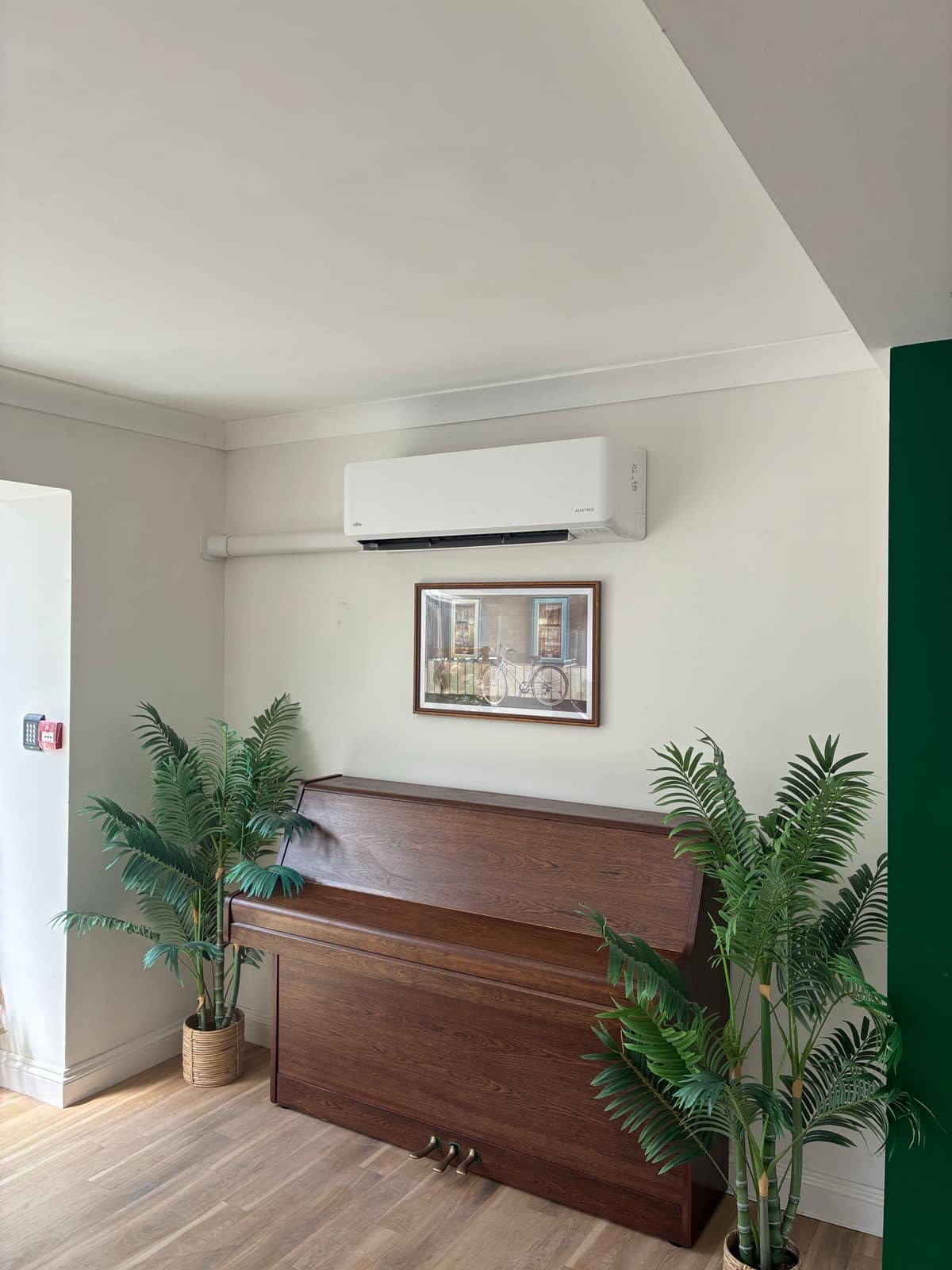 Wall-mounted air conditioning unit installed above a piano in a domestic room
